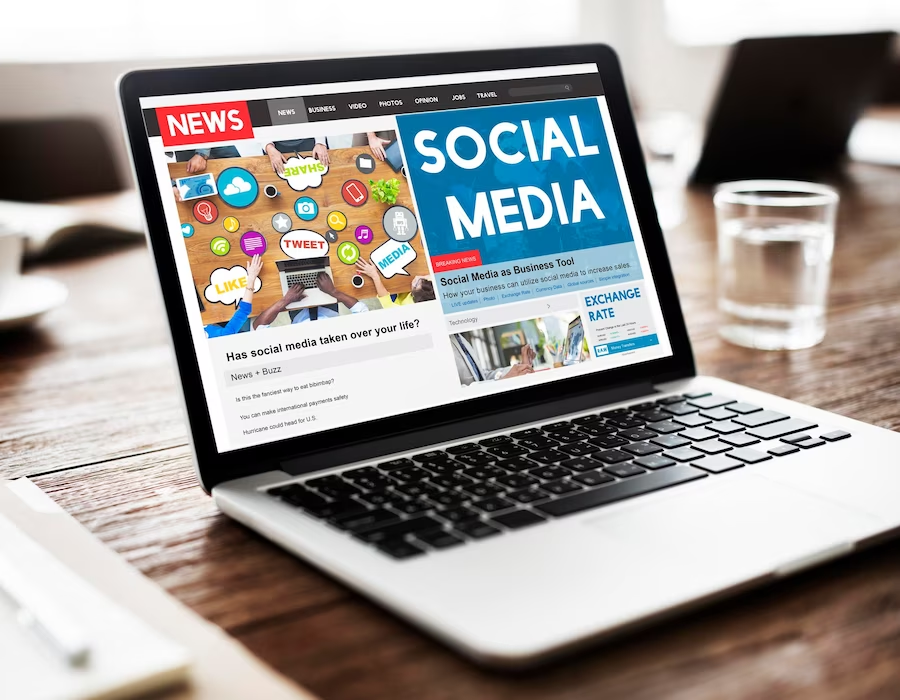 A laptop resting on a table displaying the words 'news' and 'social media' on the screen